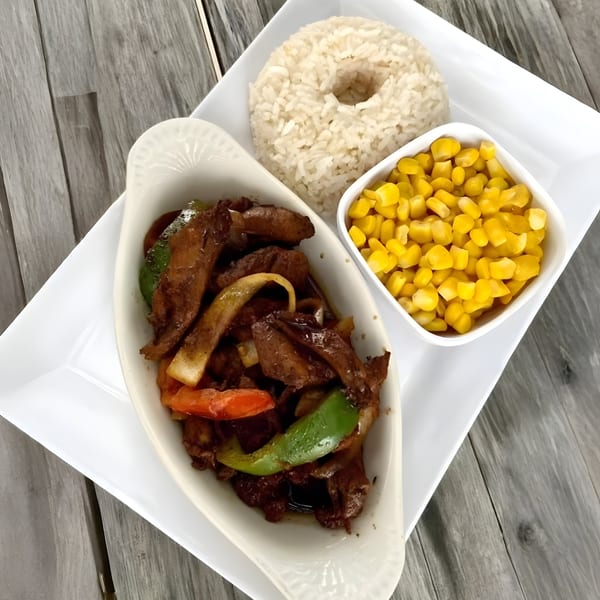 Latin Chicks' steak with peppers and onions, rice, and corn on a white plate.