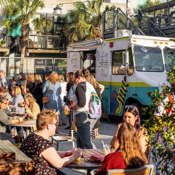 People gather around the Latin Chicks food truck, enjoying food and drinks at outdoor tables.