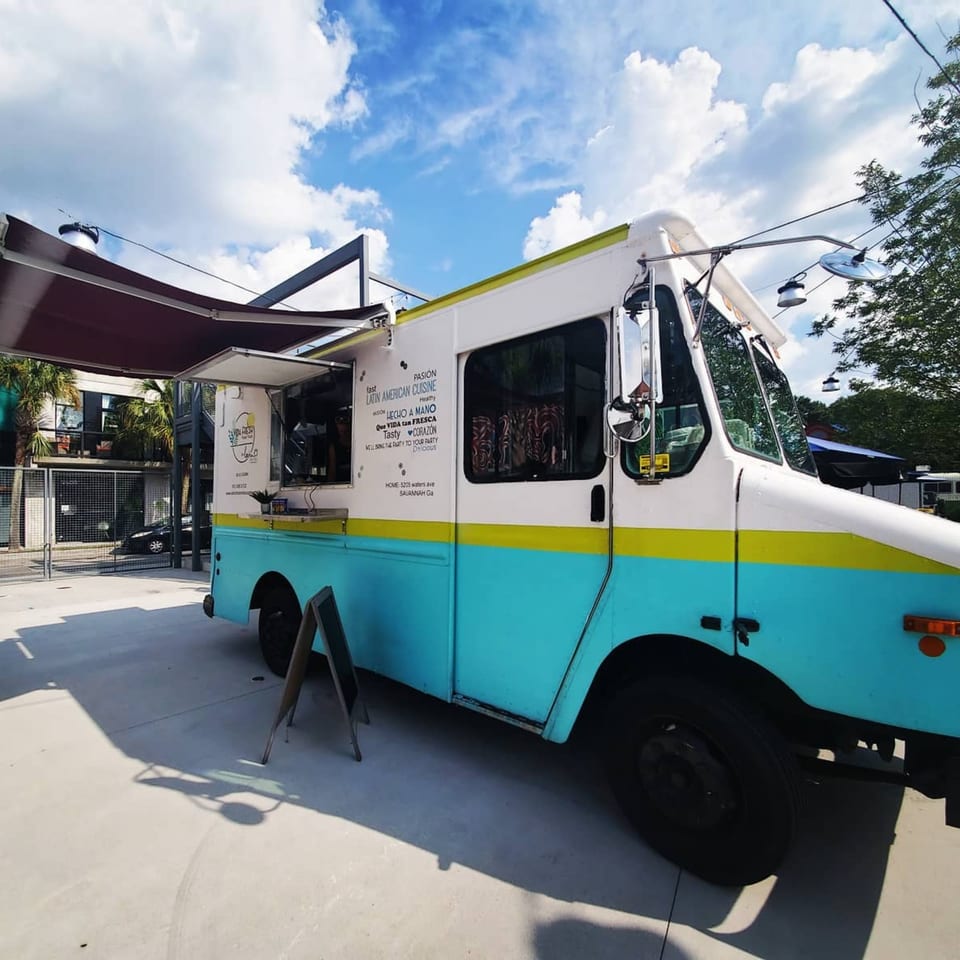 Latin Chicks food truck, white and teal with a yellow stripe, parked outdoors under a blue sky.