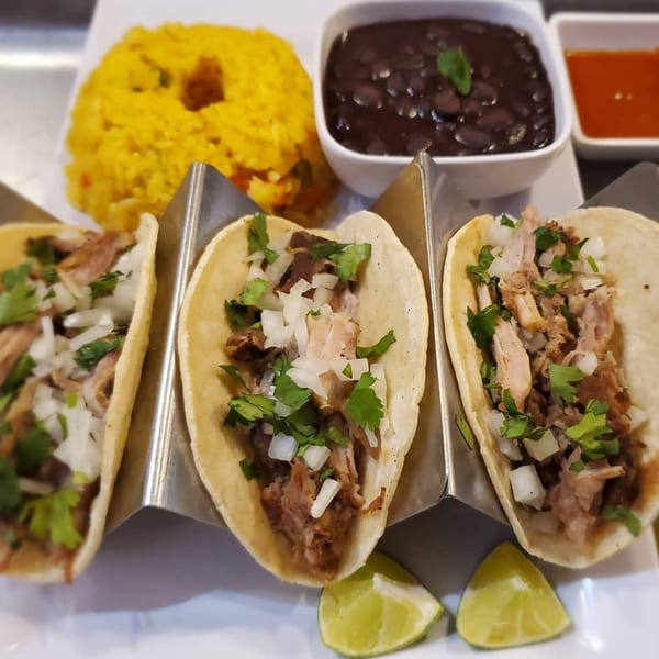 Three Latin Chicks tacos with meat, onions, and cilantro, served with yellow rice, black beans, and lime.