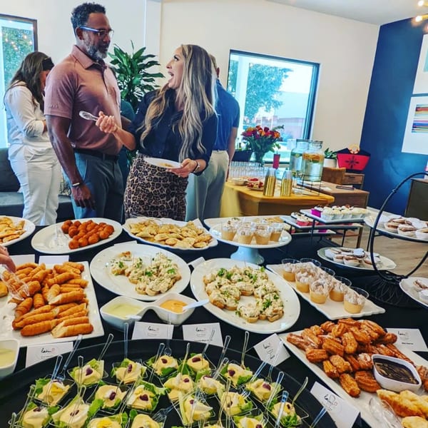 Guests gather around a buffet table laden with various Latin Chicks appetizers and desserts.