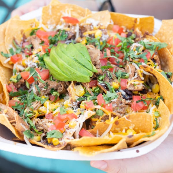 A large plate of Latin Chicks nachos with pulled pork, cheese, tomatoes, corn, and avocado.