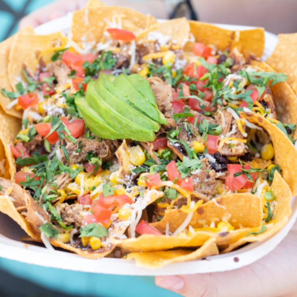 A large plate of Latin Chicks nachos with pulled pork, cheese, tomatoes, corn, and avocado.