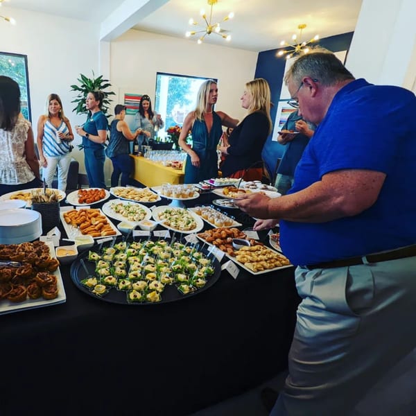 Guests mingle around a buffet table laden with various Latin American appetizers and desserts.