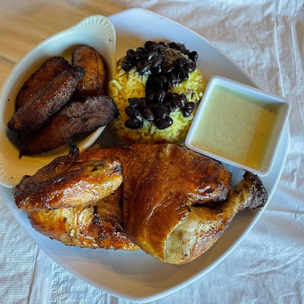 A Latin Chicks meal with roasted chicken, yellow rice, black beans, fried plantains, and green sauce.
