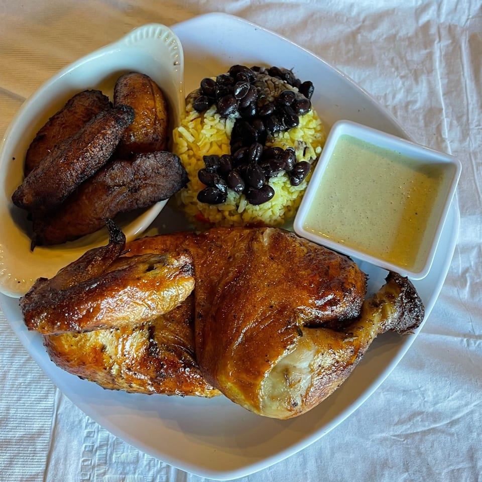A Latin Chicks meal with roasted chicken, yellow rice, black beans, fried plantains, and green sauce.