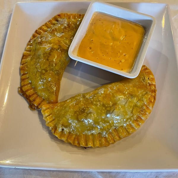 Two golden-brown Latin American empanadas with crimped edges, served with a side of orange dipping sauce.