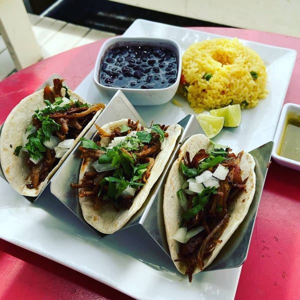 Three Latin Chicks tacos with shredded meat, onions, cilantro, rice, black beans, and lime.
