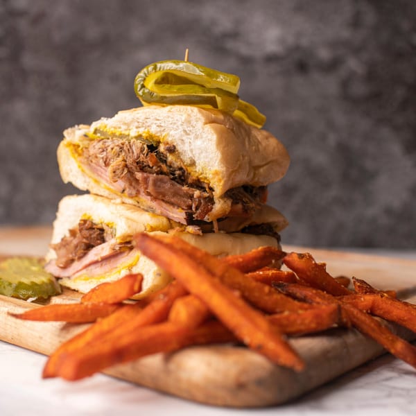 A Latin Chicks Cuban sandwich with pulled pork, ham, cheese, mustard, and pickles, served with sweet potato fries.