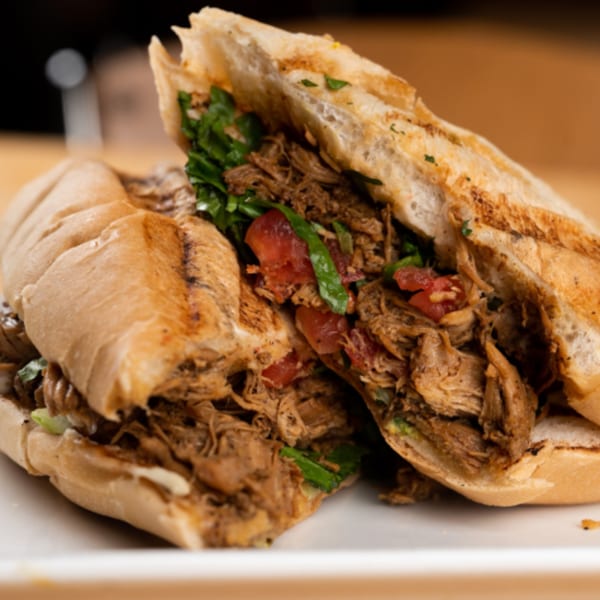 A Latin Chicks Latin-American sandwich, cut in half, filled with shredded meat, lettuce, and tomatoes.