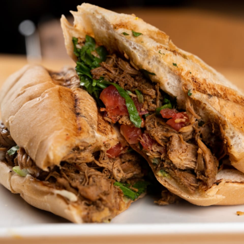 A Latin Chicks Latin-American sandwich, cut in half, filled with shredded meat, lettuce, and tomatoes.