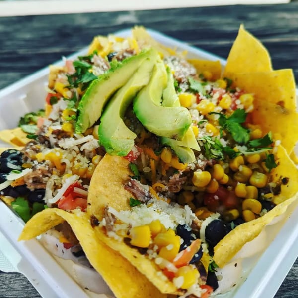 Latin Chicks' nachos with avocado, corn, black beans, and shredded meat in a white container.