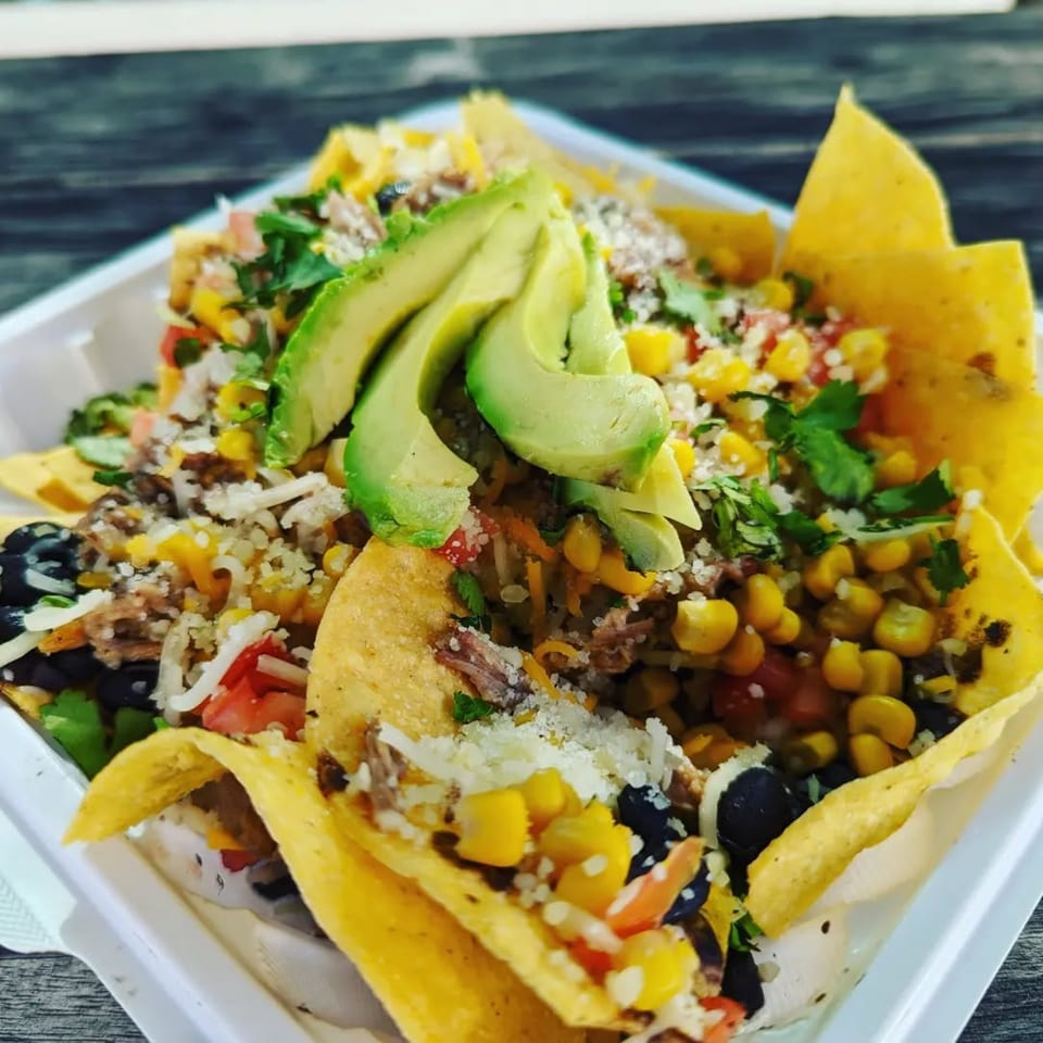 Latin Chicks' nachos with avocado, corn, black beans, and shredded meat in a white container.
